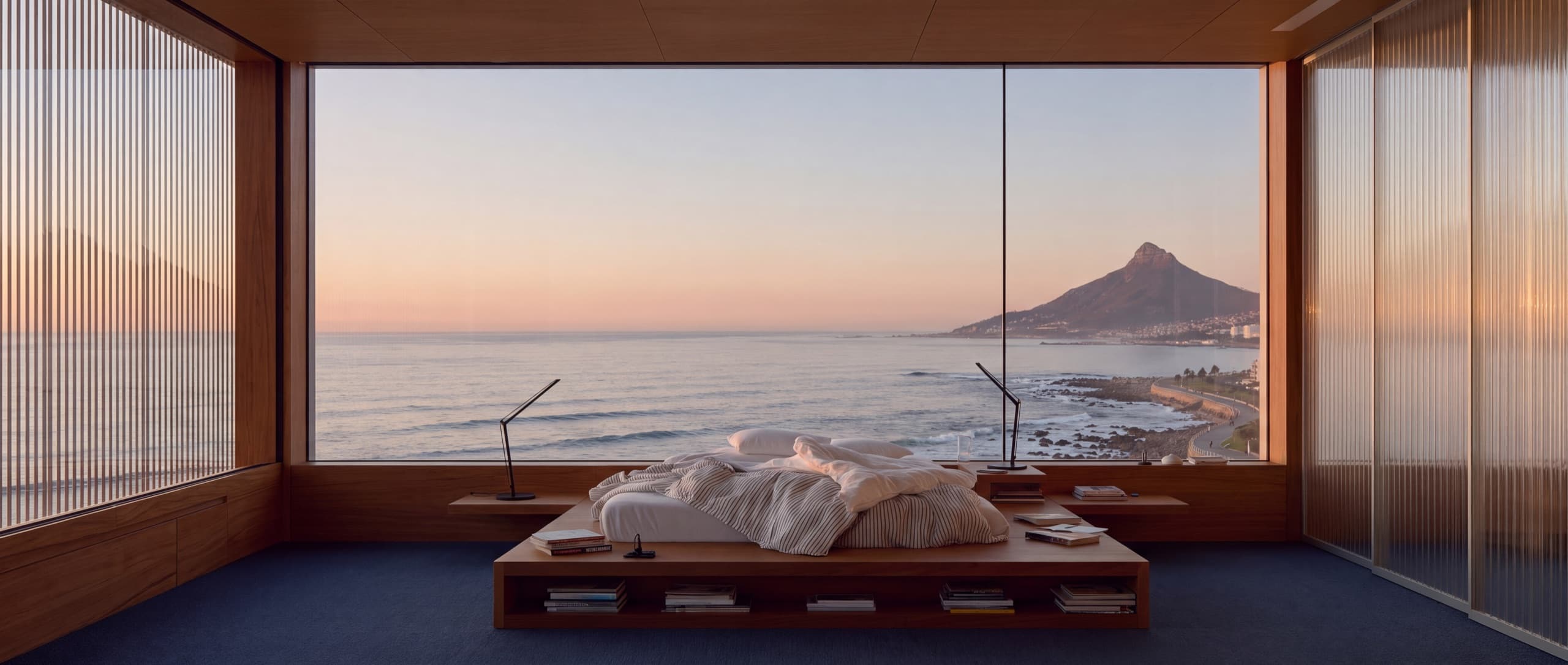 Bedroom with a wall of glass overlooking the ocean at sunset