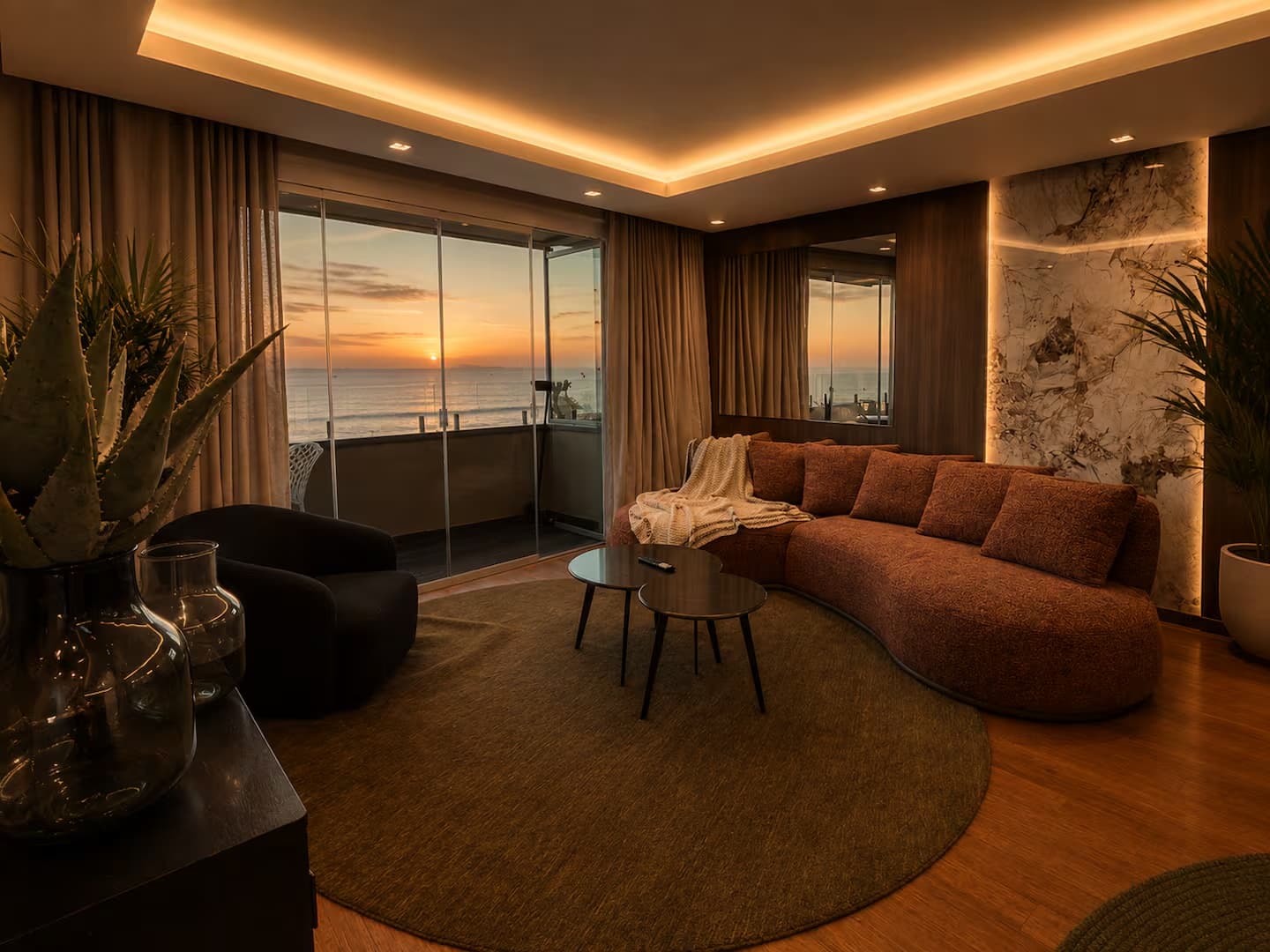 Living room with a curved rust sofa and a glass door opening onto an ocean sunset